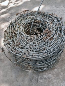 Roll of old barbed wire for fencing close-up on gray concrete in the yard.