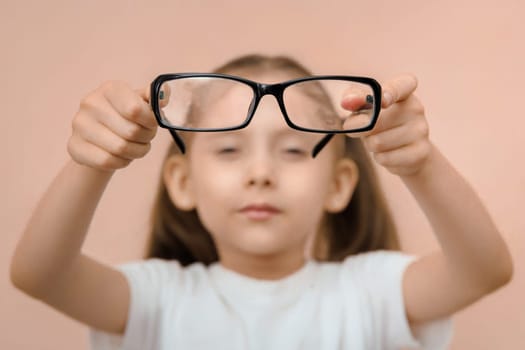Close-up portrait of an out-of-focus preschool girl holding diopter glasses in front of her in focus.