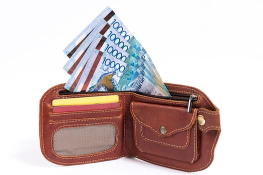 Tenge banknotes in a leather wallet on a white background.