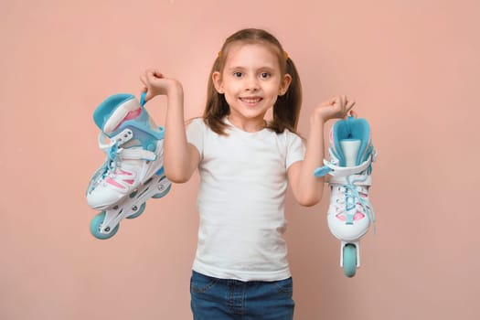 Happy smiling caucasian girl 7 years old in a white t-shirt with roller Skates on a pink background.