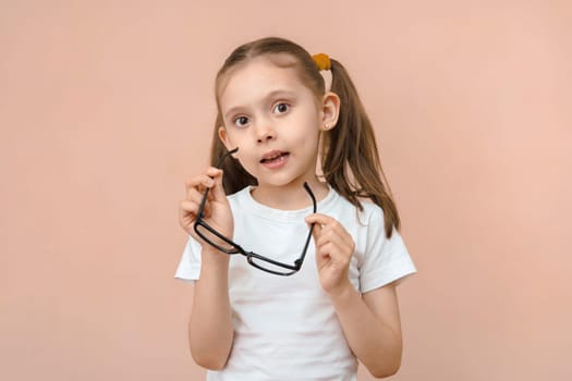 Cute caucasian elementary school age girl with poor eyesight holding diopter glasses in front of her.