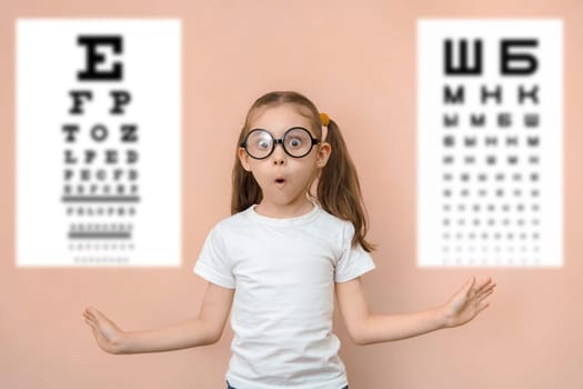 Surprised girl 7 years old in round glasses against the background of blurry tables for checking visual acuity.