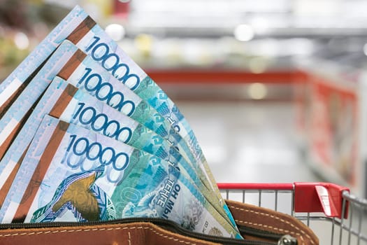 Rising prices for food products in Kazakhstan. Tenge in a wallet against the background of blurred grocery store.