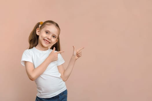 Cute smiling caucasian preschool girl in a white t-shirt points to an empty space.