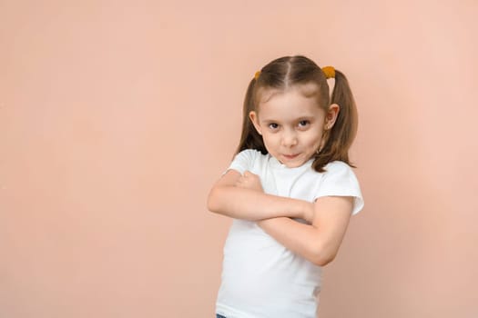 A slightly offended Caucasian girl of 7 years old crossed her arms over her chest, looks at the camera.