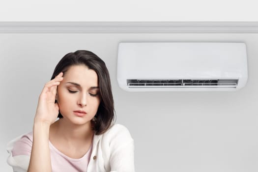 Woman holding her head while experiencing a cold and feeling unwell due to the air conditioner.