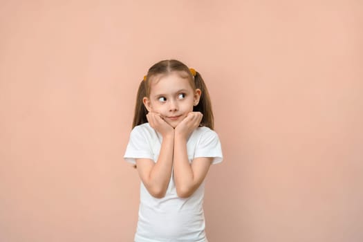 Cute caucasian preschool girl in a white t-shirt looks away.