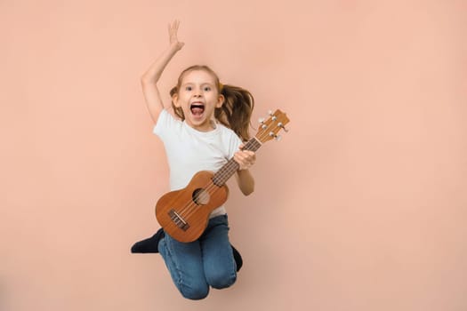 Emotional little jumping girl playing guitar like rock star on pink background.