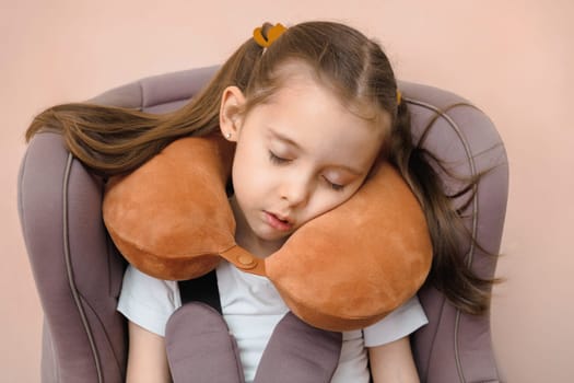 Preschool girl fastened sleeping in a car seat with travel pillow.