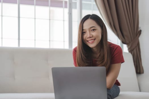 Satisfied asian woman relaxing on comfortable couch, using laptop at home, happy girl chatting with friends in social network, spending lazy weekend, watching movie, shopping online, writing email..