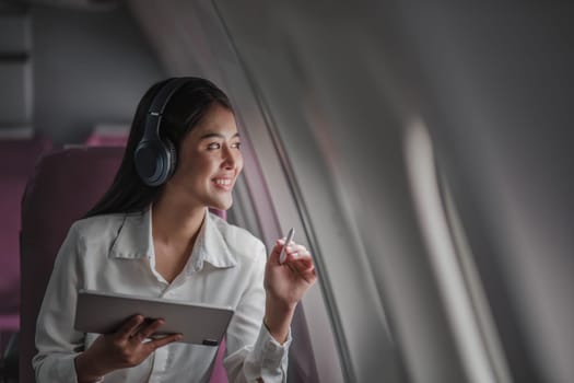 Asian young woman using tablet sitting near windows at first class on airplane during flight,Traveling and Business concept..