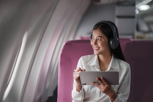 Asian young woman using tablet sitting near windows at first class on airplane during flight,Traveling and Business concept..