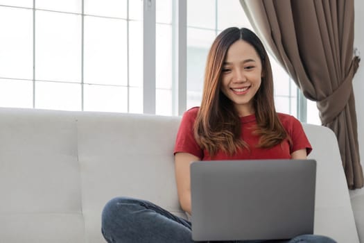 Satisfied asian woman relaxing on comfortable couch, using laptop at home, happy girl chatting with friends in social network, spending lazy weekend, watching movie, shopping online, writing email..