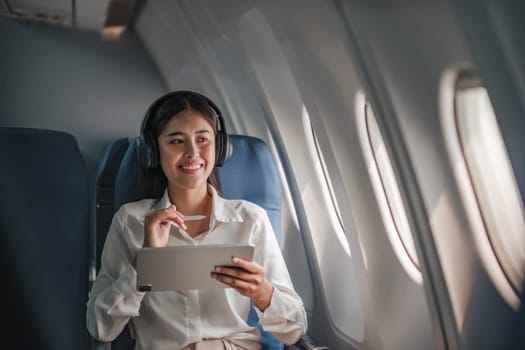 Asian young woman using tablet sitting near windows at first class on airplane during flight,Traveling and Business concept..