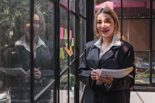 Young businesswoman creative team using post it notes in glass wall to writing strategy business plan to development grow to success...