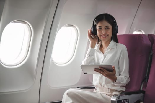 Asian young woman using tablet sitting near windows at first class on airplane during flight,Traveling and Business concept..