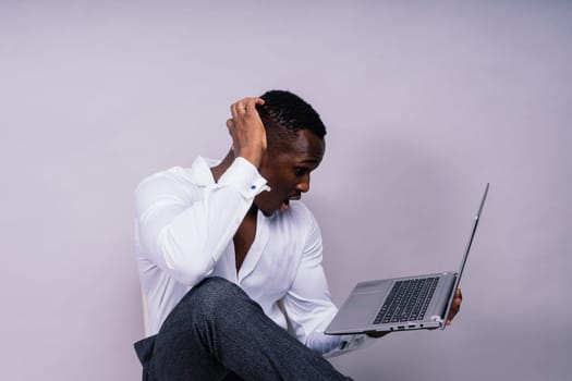 Optimistic african-american male student in a casual shirt using laptop pc isolated