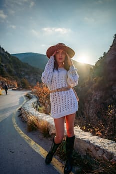 Woman road mountain. A woman in a white sweater, black boots and a hat walks along a winding alpine path between the mountains at sunset in late summer. The concept of travel