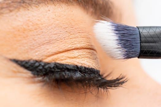 Close up woman applying a shadow with make up brush on the eyelid.