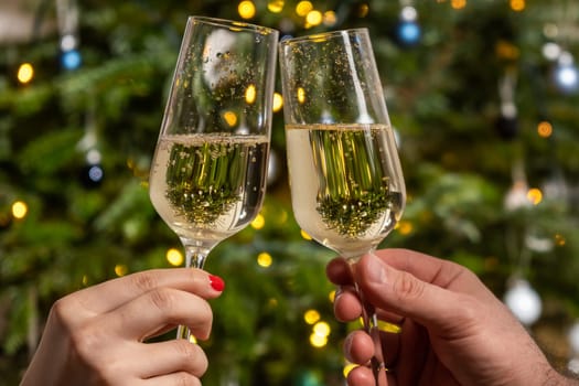 Man and woman clinking glasses with champagne against the Christmas tree. Celebrating the atmosphere of the New Year party.