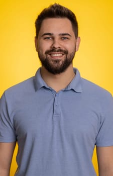 Portrait of happy calm caucasian man smiling friendly, glad expression looking at camera dreaming resting, relaxation feel satisfied concept good news celebrate win. Guy on yellow background. Vertical