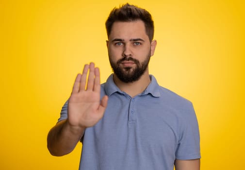 Angry man say No hold palm folded crossed hands in stop gesture, warning of finish, prohibited access, declining communication, body language, danger. Young guy on yellow background. People lifestyle