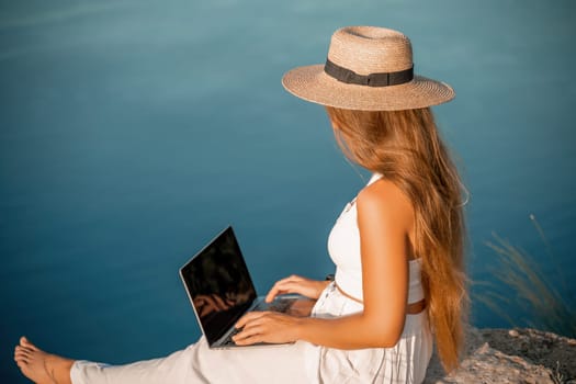 Freelance women sea working on the computer. Good looking middle aged woman typing on a laptop keyboard outdoors with a beautiful sea view. The concept of remote work