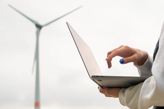 Close up woman uses a laptop to control the work of the windmill against the grey sky.