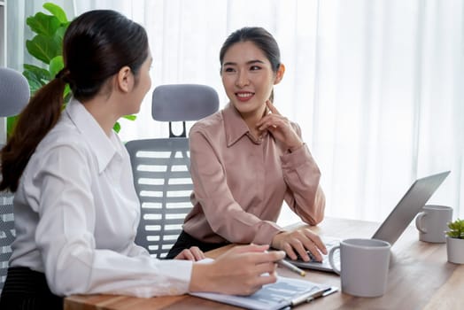 Two young office lady colleagues collaborating in modern office workspace, engaging in discussion and working together on laptop, showcasing their professionalism as modern office worker. Enthusiastic