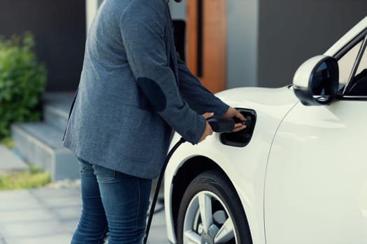 Closeup progressive asian man install cable plug to his electric car with home charging station. Concept of the use of electric vehicles in a progressive lifestyle contributes to clean environment.