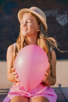 Portrait of a girl in a hat with a pink balloon. She is dressed in pink clothes and her hair is long and loose