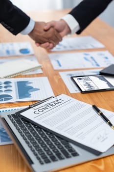 Closeup professional businessman shaking hands over desk in modern office after successfully analyzing pile of dashboard data paper as teamwork and integrity handshake in workplace concept. fervent