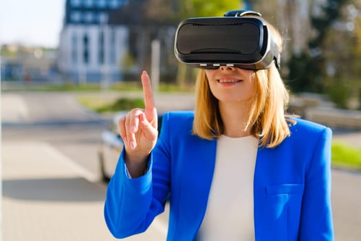 A happy woman in the suit is standing outside and gestures in augmented reality in 3D VR goggles.