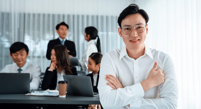 Portrait of focus young successful confident male manager, executive wearing business wear in harmony office arm crossed with blurred meeting background of colleagues, office worker.