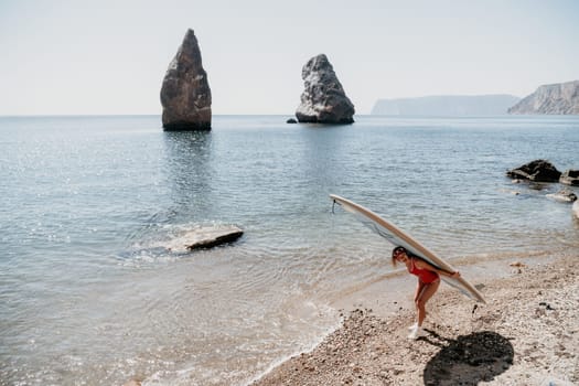 Close up shot of beautiful young caucasian woman with black hair and freckles looking at camera and smiling. Cute woman portrait in a pink bikini posing on a volcanic rock high above the sea