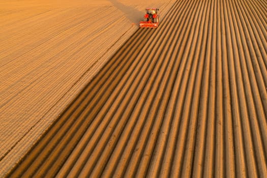 Aerial view of tractor making furrows on soil at agricultural field at sunset, April 2022, Prague, Czech Republic