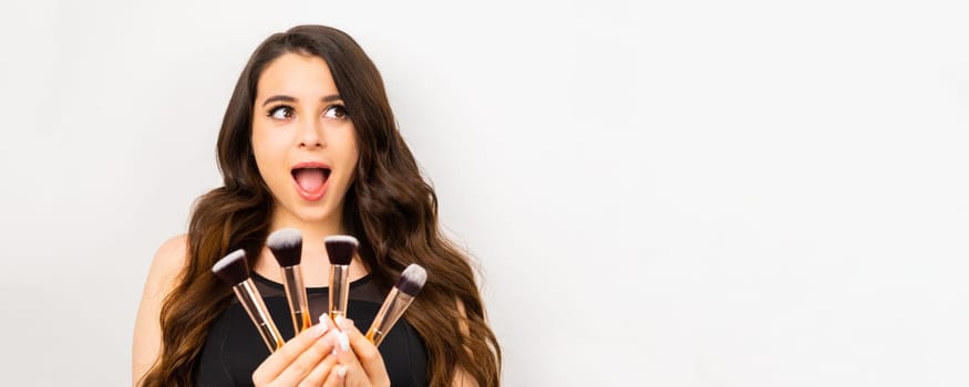 Attractive excited woman holding a set of makeup brushes for professional use.