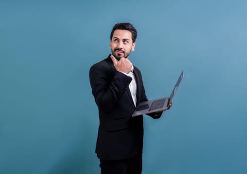 Successful businessman in black suit with innovative tech concept, standing pose and holding laptop and smiling with excitement on copyspace background for promotion or advertisement. Fervent