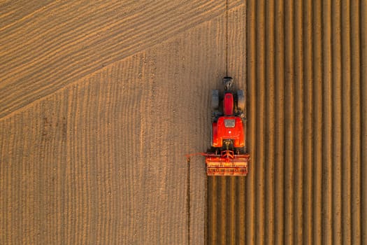 PRAGUE , CZECH REPUBLIC - MARCH 18 2022: Tractor drives preparing beds for planting seedlings in cultivated soil. Heavy machine tills on field helping with agriculture aerial view