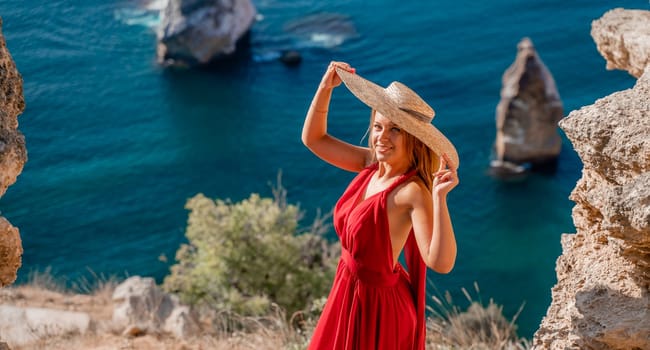 A woman in a flying red dress fluttering in the wind and a straw hat against the backdrop of the sea