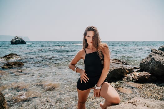 Woman travel sea. Young Happy woman in a long red dress posing on a beach near the sea on background of volcanic rocks, like in Iceland, sharing travel adventure journey