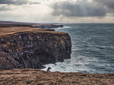 Cold sea water crashing against rocks near rough stony cliffs, on stormy day in Iceland