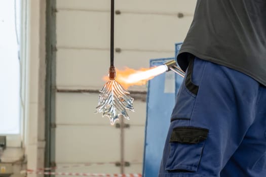 A man uses a gas burner to melt glass. A craftsman makes a glass in a leaf shaped.