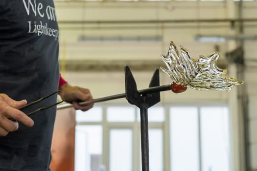 Close up man makes a leaf from the glass for vase or chandelier using tongs and blowpipe.