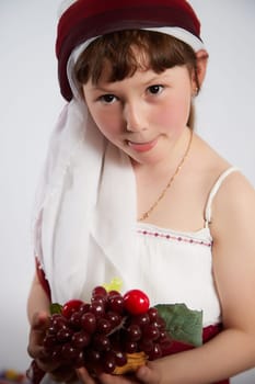 Portrait of Little girl in a stylized Tatar national costume with berries and a brush of grapes on a white background in the studio. Photo shoot of funny young teenager who is not a professional model