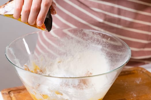 Close up woman sifts wheat flour through a sieve into mixing bowl for dough preparation for cake and bakery on the black background. Knead the dough for homemade pastry.