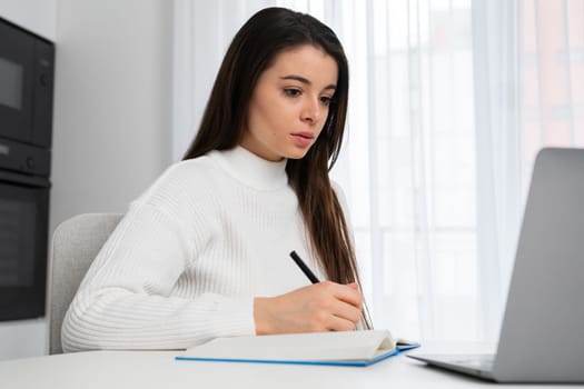 Portrait of a pensive young student making notes to the textbook during e learning.