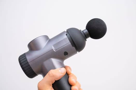 Electric massager gun in mans hand on the white background. Recovery after a workout.