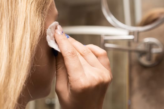 Young woman removes makeup with a cotton pad from her face in the bathroom.