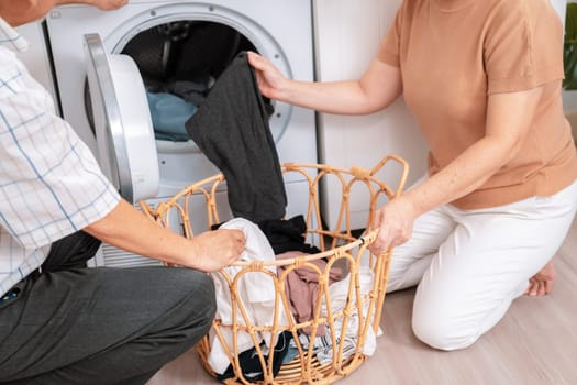 Senior couple working together to complete their household chores at the washing machine in a happy and contented manner. Husband and wife doing the usual tasks in the house.